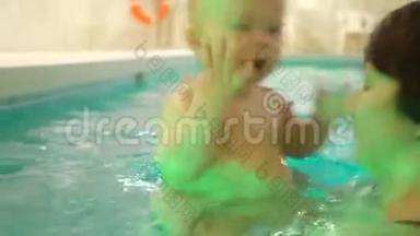 一位年轻的母亲带着一个小男孩游泳，在游泳池里玩得很开心。 快乐的小男孩和他一起在游泳池里游泳